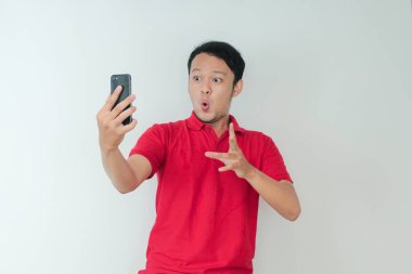 Genç Asyalı adamın yüzü, gri arka planda akıllı telefonda gördüklerini şok etti..