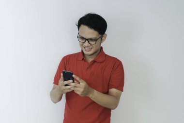 Zeki Asyalı genç adam stüdyo arka planında akıllı telefon kullanırken mutlu ve gülümsüyor.