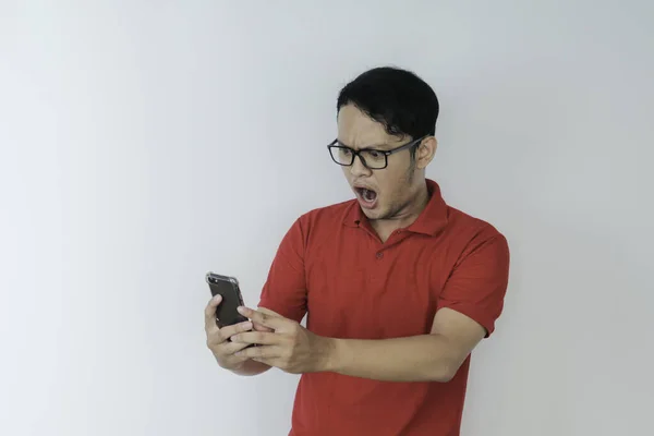 若いアジア人の男のすごい顔は 彼が孤立した灰色の背景にスマートフォンで見たものをショックを受けました — ストック写真
