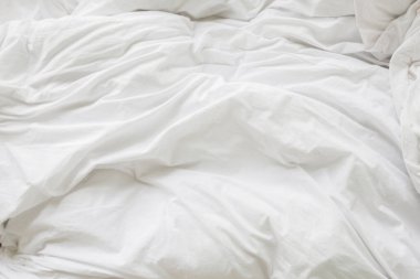 Yatak odasındaki kırışık, dağınık battaniye ve beyaz yastık sabah uyandıktan sonra, uzun bir gece uyuduktan sonra, yorgan ve battaniyenin ayrıntıları, otel odasında beyaz battaniyeli yapılmamış bir yatak..