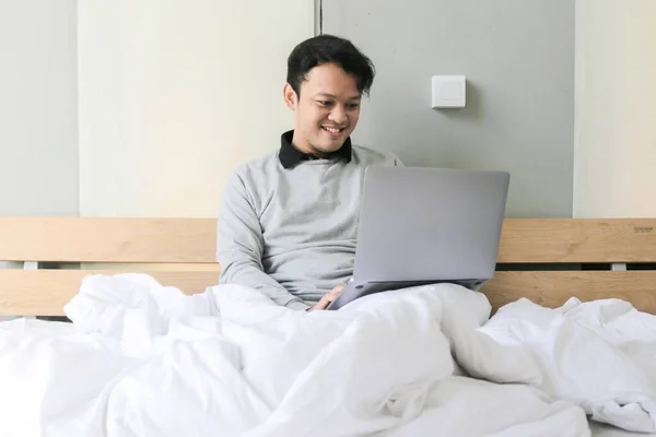 Homem Asiático Feliz Está Trabalhando Com Seu Laptop Sua Cama — Fotografia de Stock