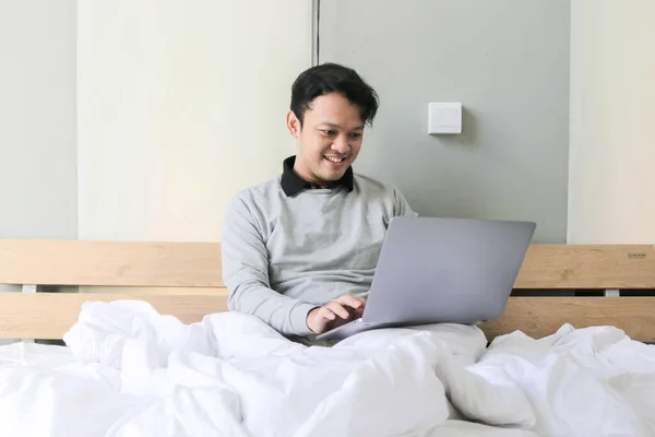 Homem Asiático Feliz Está Trabalhando Com Seu Laptop Sua Cama — Fotografia de Stock