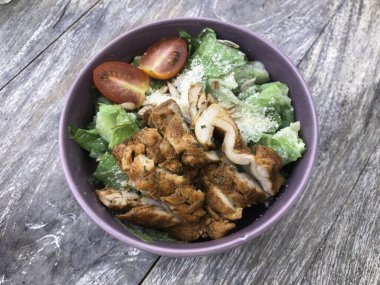 Yeşil yapraklı yeşil vejetaryen salatası karışımı, sebzeler, tavuk katsu dilimleri. Gri ahşap masadaki üst manzara.