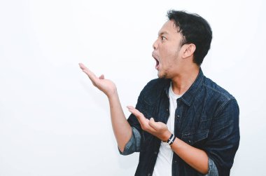 Genç Asyalı adam şaşırdı ve haykırdı vay canına sağ elini gri arka planda tek başına gösterdi..