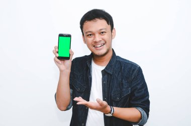 Genç Asyalı adam ayakta duruyor ve gülümsüyor beyaz arka planda yeşil ekranda akıllı telefon ekranında.