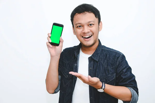 Ung Asiatisk Man Står Och Ler Pekar Grön Skärm Smartphone — Stockfoto