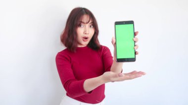 Şok Asyalı güzel kız beyaz arka planda yeşil ekrandaki telefonu gösteriyor.