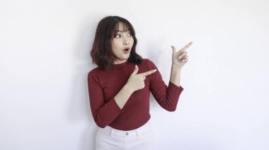 Şok edici Asyalı güzel kız beyaz arka planda kırmızı gömlekli kızı işaret ediyor.