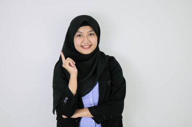 Başörtüsü takan Asyalı genç kadın gülümsüyor ve onu işaret ediyor..