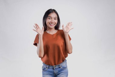 Kahverengi tişörtlü neşeli Asyalı kadın elini sallıyor. Beyaz arka planda izole bir şekilde selam veriyor..