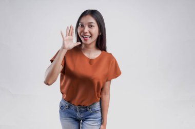 Heyecanlı genç Asyalı kadın bağırıyor ve çığlık atıyor. Elleri ağzında, beyaz arka planda soyutlanmış..