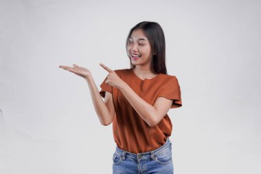 Kahverengi gömlekli güzel bir Asyalı kadın ellerindeki fotokopi alanını işaret ediyor, beyaz arka planla izole edilmiş..