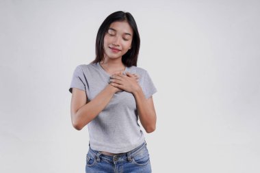 Gri tişörtlü mutlu, düşünceli, genç Asyalı kadın izole edilmiş beyaz arka planda rahatlamış ve gülümsüyor..