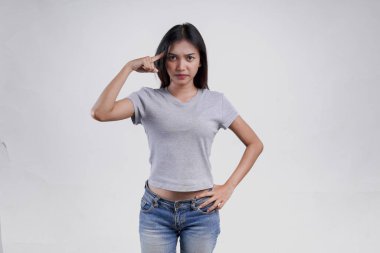 Gri tişörtlü düşünceli genç Asyalı kadın ciddi görünüyor. Sıkı düşünüyor, beyaz arkaplan tarafından izole edilmiş..