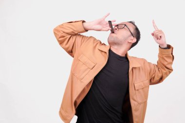 Heyecanlı genç Asyalı adam beyaz arka planla izole edilmiş fotokopi alanını işaret ederken elektrikli sigara içiyor..