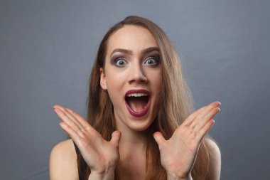 Gri arka planda parlak makyajlı hayrete düşmüş bir kızın fotoğrafı.