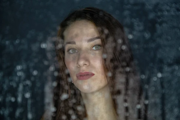 Portrait de jeune femme derrière un verre avec des gouttes d'eau — Photo