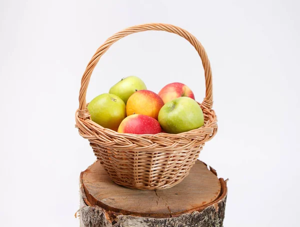 Red and green apples in wicker basket on wooden stump — Stock Photo, Image