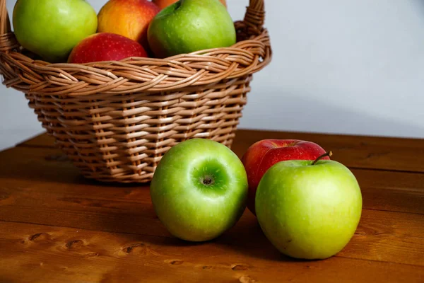 在木板上的柳条篮里打红、绿苹果 — 图库照片