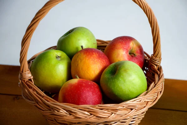 Rode en groene appels in rieten mandje op houten plank — Stockfoto