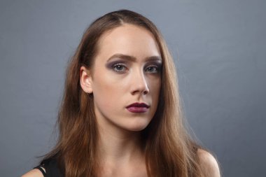 Gri arka planda parlak makyajlı genç bir kadın.