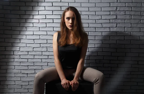 Photo de jeune femme assise sur fond de mur de briques — Photo