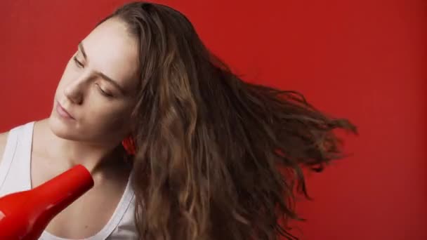 Video de mujer caucásica secando el pelo largo sobre fondo rojo — Vídeos de Stock
