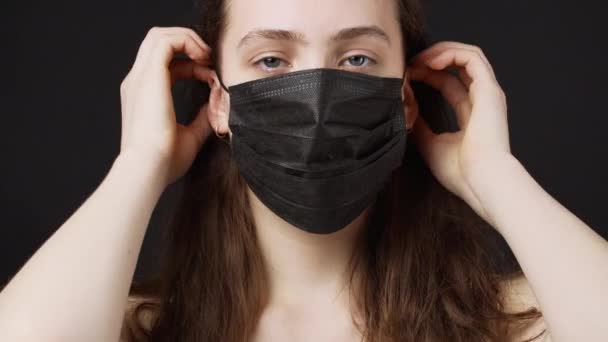 Video af kvinde dressing sort medicinsk maske på sort baggrund – Stock-video