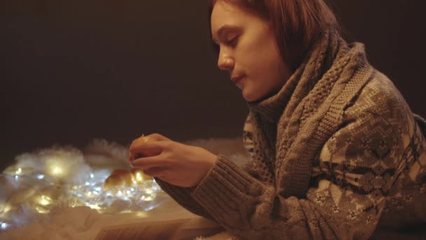 Video of reading girl in knitted sweater peeling tangerine — Stock Video