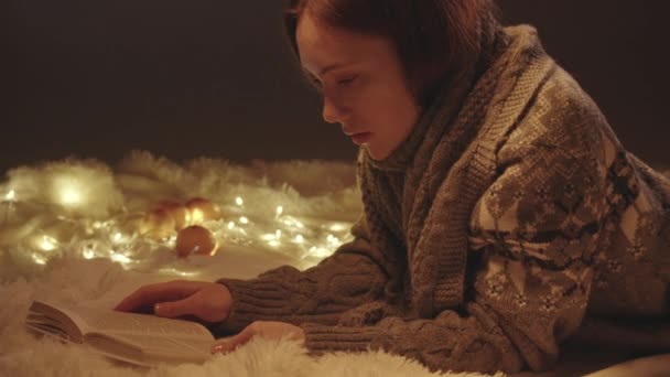 Reading girl in knitted sweater among Christmas lights — Stock Video