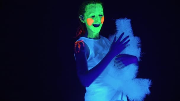 Fotografowanie tańczącej kobiety z malowaną twarzą i choinką w świetle ultrafioletowym — Wideo stockowe