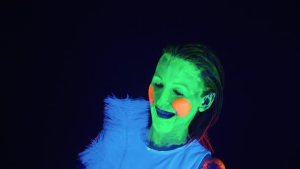 Танцююча жінка з пофарбованим обличчям і ялинкою в ультрафіолетовому світлі — стокове відео