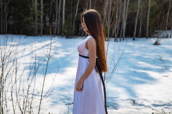 Foto de niña en un vestido blanco de perfil entre la nieve en primavera día soleado — Foto de Stock