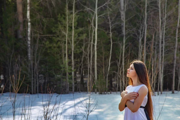 Дівчина в білій сукні з головою вгору і руками схрестилася серед снігу в лісі — стокове фото