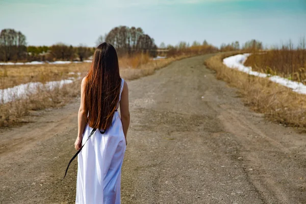 Фото молодої дівчини в білій сукні, що йде по дорозі — стокове фото