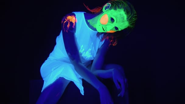 Сидяча жахлива жінка з пофарбованим обличчям в ультрафіолетовому світлі — стокове відео