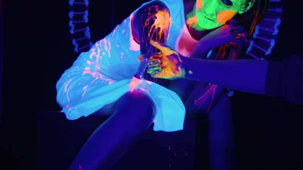 Erschießung einer Frau mit Flüssigfarbe auf ihrem Körper in UV-Licht — Stockvideo