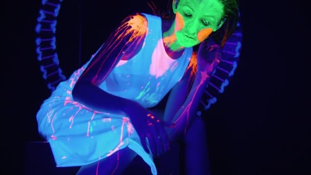 Sitzende bemalte Frau mit beängstigendem Make-up im UV-Licht — Stockvideo