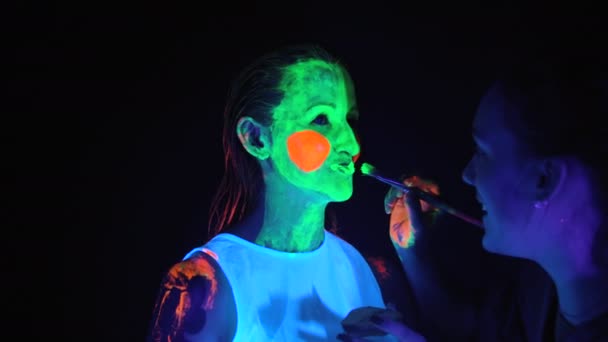 Mädchen tragen Farbe auf das Gesicht der Models im UV-Licht auf — Stockvideo