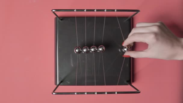 Vídeo de mulheres mão começou newtons bolas no fundo rosa, vista superior — Vídeo de Stock