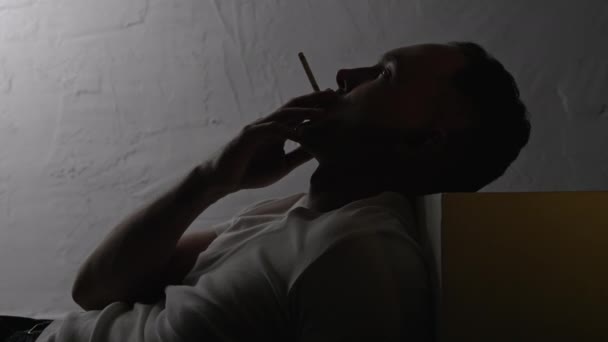 Видео лежащего курильщика с сигаретой в тени — стоковое видео