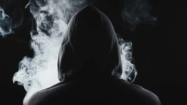 Arka kaputta sigara içen adamın fotoğrafı.