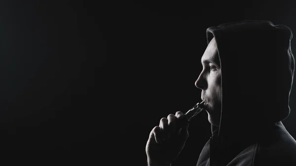 Hombre con el cigarrillo electrónico en capucha en negro — Foto de Stock