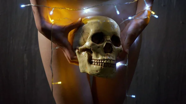 Naked girl with Christmas lights holding human skull — Stock Photo, Image