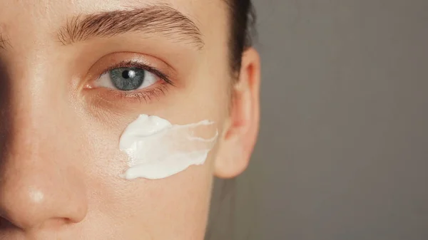 Jonge vrouw zet een witte crème op haar gezicht — Stockfoto