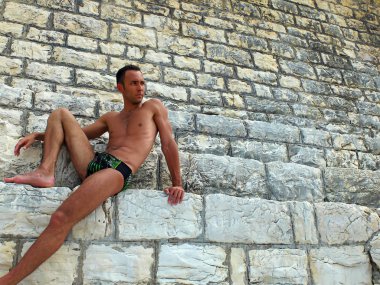 Taş duvara oturan genç esmer adam