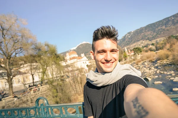 Joven hombre guapo tomando selfie por el río Passer en el casco antiguo de Meran en el Tirol del Sur en Italia - Concepto de aventura y estilo de vida de viaje - Composición con horizonte inclinado y tonos cálidos de color de la tarde —  Fotos de Stock