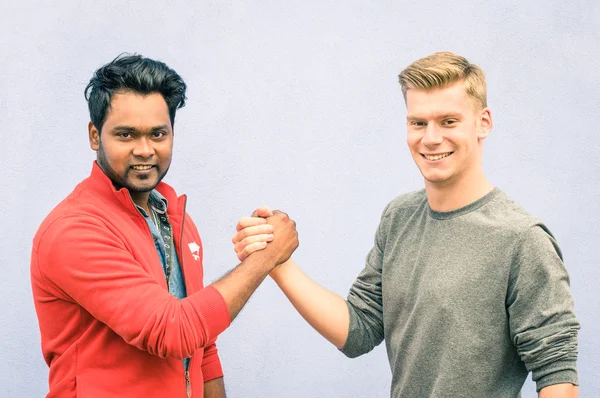 Индийские и кавказские мужчины пожимают руки современными рукопожатиями, чтобы показать друг другу дружбу и уважение - Лучшие друзья, имеющие армрестлинг против расизма на голубой стене - Мягкий обессыщенный отфильтрованный взгляд — стоковое фото