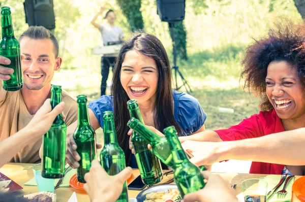 Multiracial friends having fun at barbecue garden party - Friendship concept with young happy people cheering beer bottles at summer picnic - Vintage cross processed filter with focus on middle girl — Stock Photo, Image