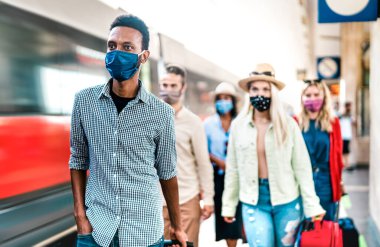 Tren istasyonu platformunda yürüyen çok ırklı insanlar - Yeni normal seyahat konsepti koruyucu maske takmış genç gezginler - soldaki Afrikalı Amerikalı adama odaklan